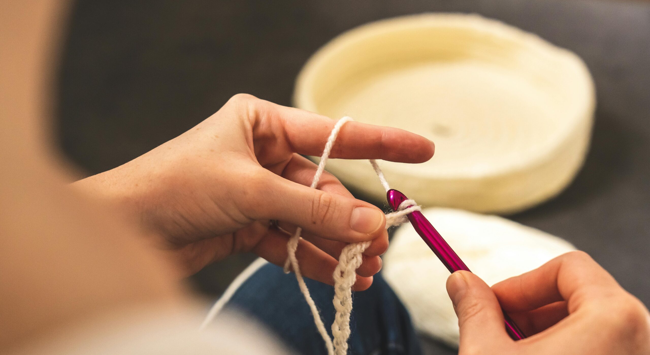 A focused shot of hands crocheting with a pink hook and white yarn, showcasing the art of crafting.